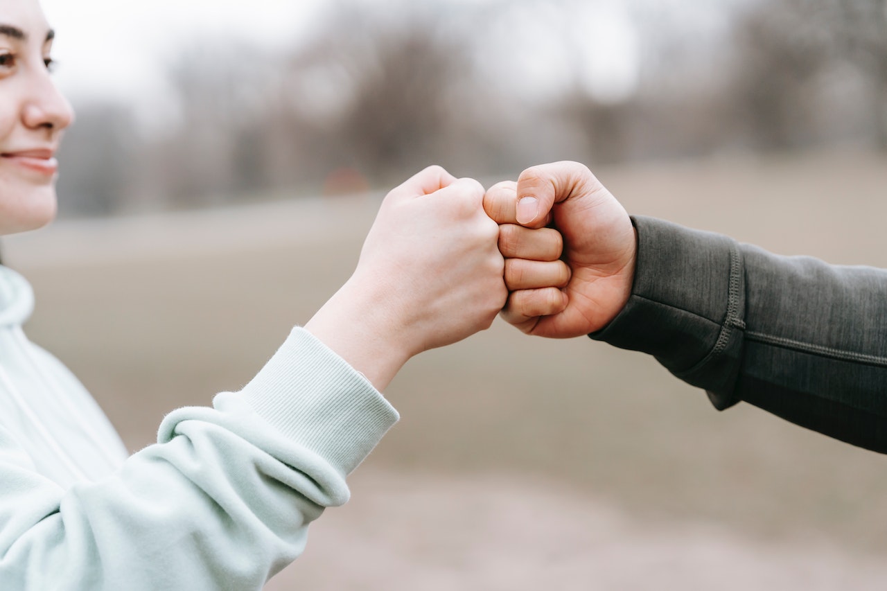 Two hands performing a fist bump outdoors, symbolizing trust and connection.